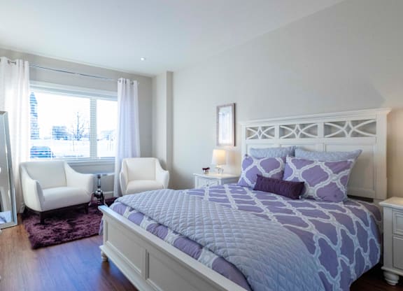 A bedroom with a large bed and two chairs.