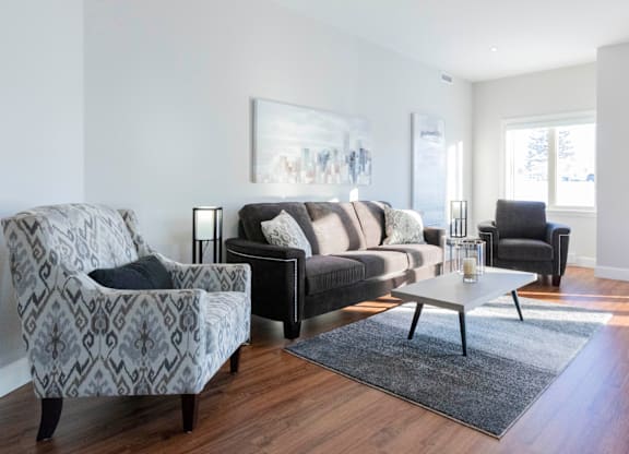 A living room with a grey patterned armchair, a black couch, and a coffee table.