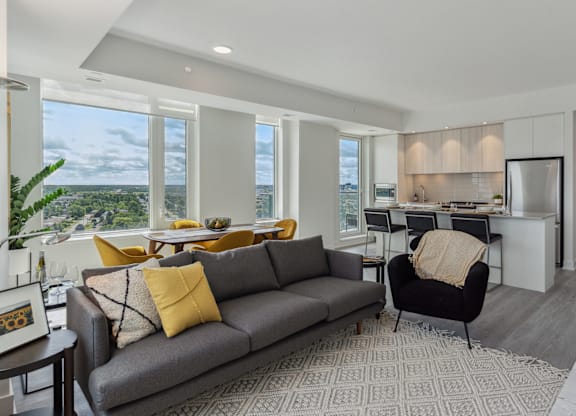 A grey couch with yellow pillows sits in a living room with a view of the city.