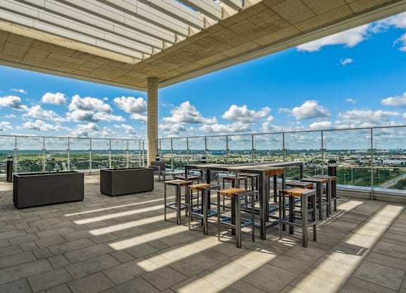 A rooftop patio with a bar and chairs overlooking a cityscape.