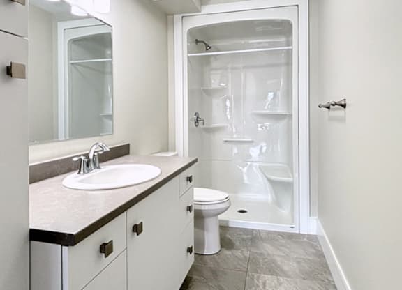 A white bathroom with a sink, toilet, and shower.