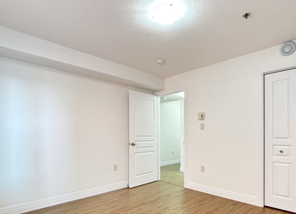 A room with white walls and wooden flooring, featuring a door and a window.