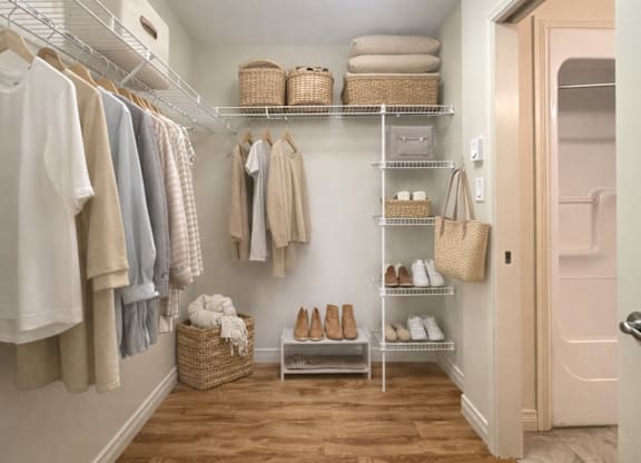 A hallway with a white wall and a white door with a shelf and clothes hanging.