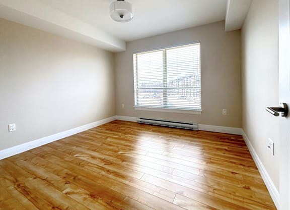 A room with wooden flooring and a window with blinds.