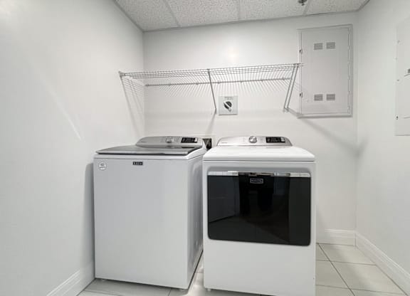 A white dishwasher and dryer in a clean, white-walled laundry room.