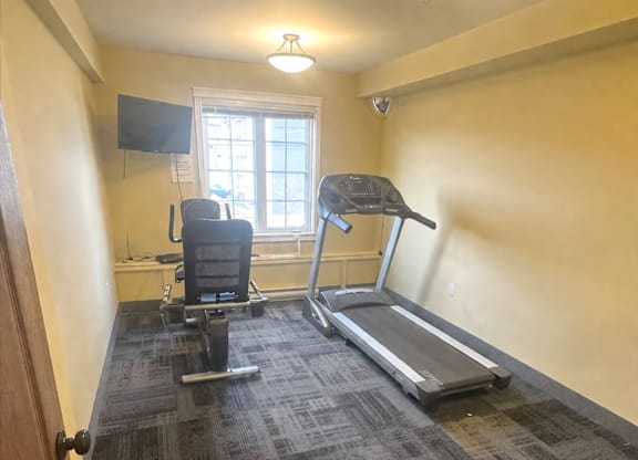 A room with a treadmill, a chair, and a television.