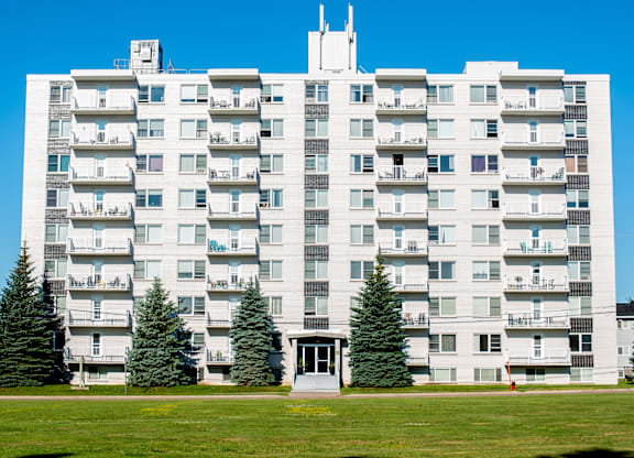 A large white apartment building with balconies and trees in front.