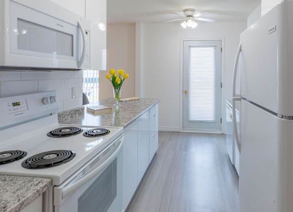 A kitchen with white appliances and a vase of yellow flowers on the counter.
