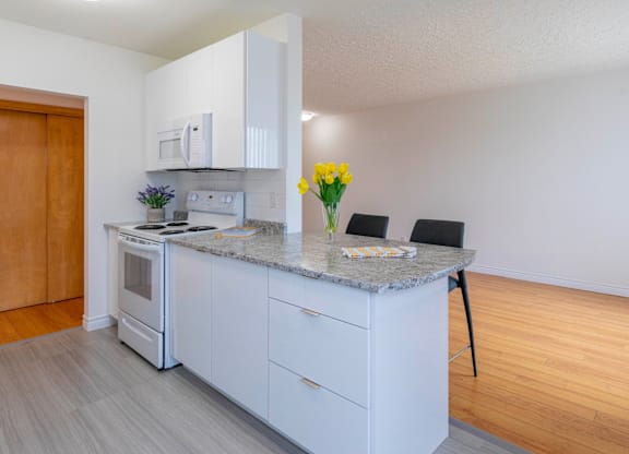 A kitchen with a white countertop and a vase of yellow flowers.