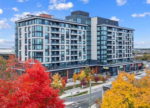 A modern multi-story building with balconies and a parking lot in front.