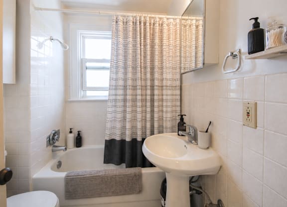 A white sink is on a white pedestal in a white tiled bathroom.