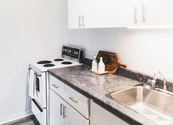 A kitchen with a stove, sink, and cabinets.