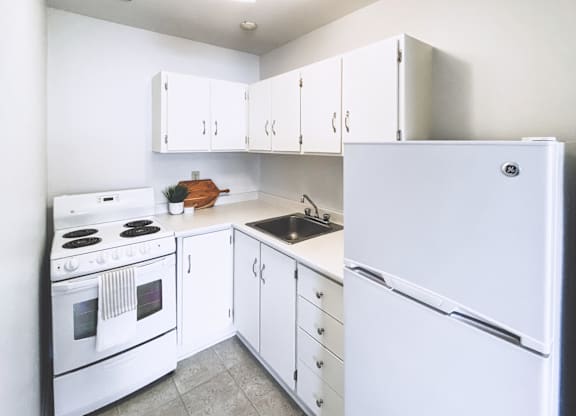A white kitchen with a refrigerator, stove, and cabinets.