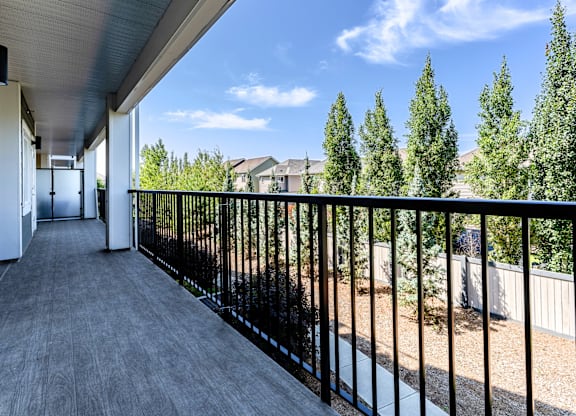 A balcony with a black railing and a view of trees and houses.