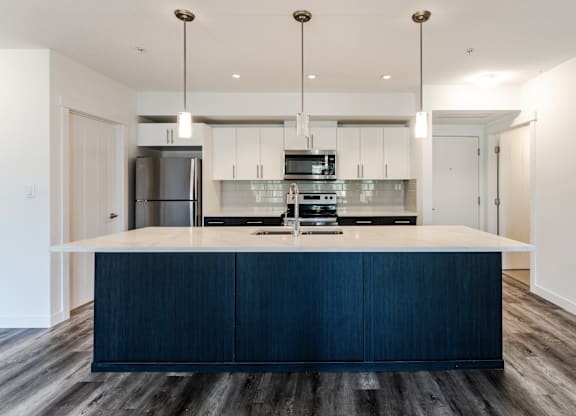 A modern kitchen with dark wood floors and white walls.