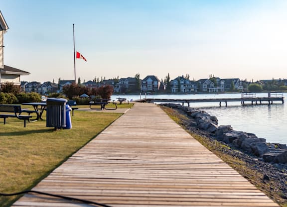 A wooden walkway leads to a body of water with a Canadian flag in the background.