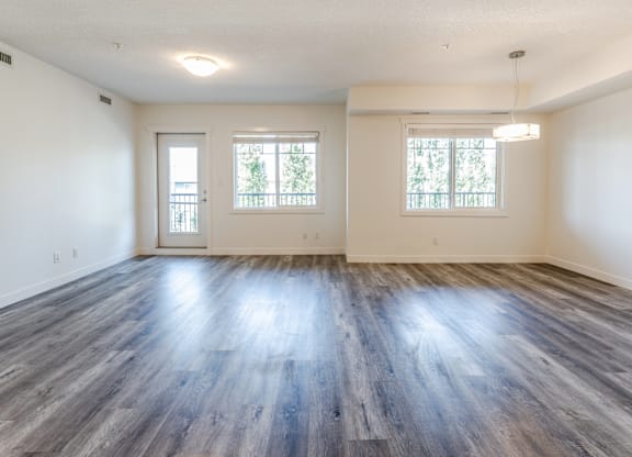 A spacious room with wooden floors and two windows.