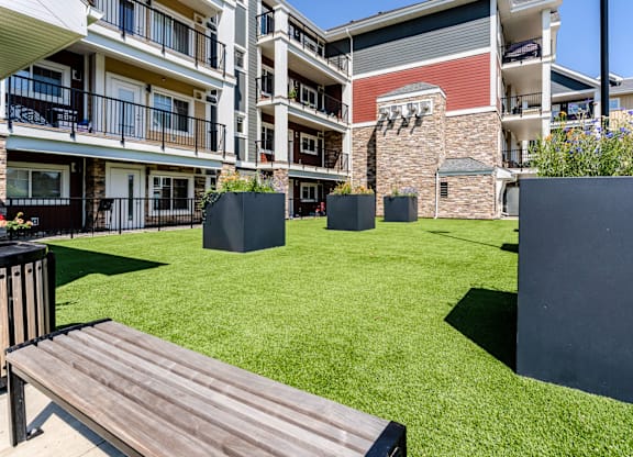 A wooden bench sits in the middle of a grassy area in front of a building.