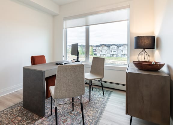 A room with a desk, chairs, and a window overlooking a residential area.