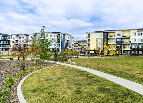A grassy area with a walkway and apartment buildings in the background.
