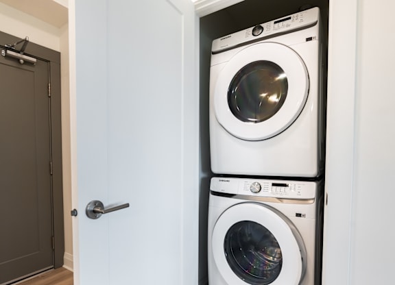 A white front load washing machine is stacked on top of another in a small laundry room.