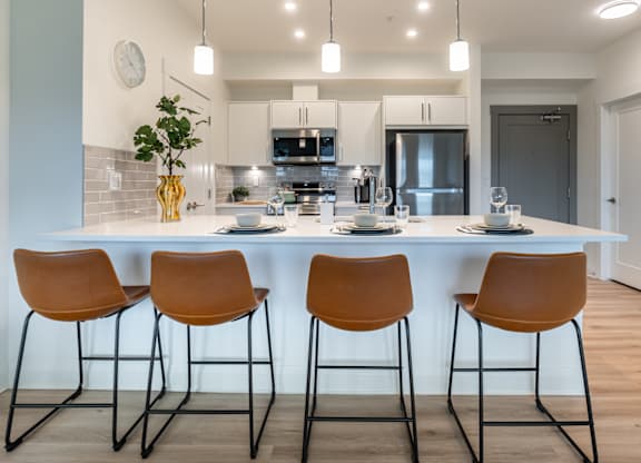 A modern kitchen with a bar area featuring a counter, four chairs, and a plant.