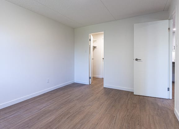 A room with white walls and wood flooring with a door on the right.