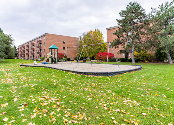 A playground with a trampoline and a slide in front of a brick building.