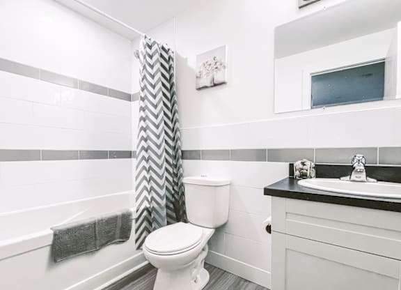 A white toilet in a bathroom with a grey and white shower curtain.