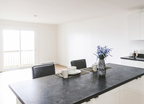 A black countertop with a vase of blue flowers and two cups on it.