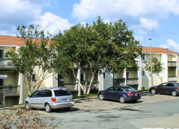 A silver minivan is parked in a parking lot in front of a white apartment building.