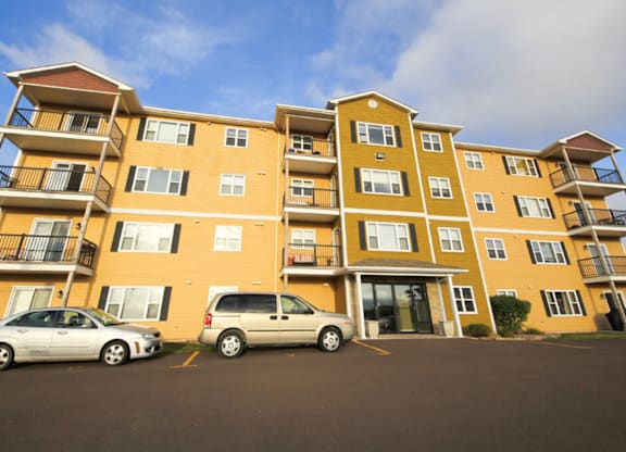 Two cars parked in front of a yellow apartment building.