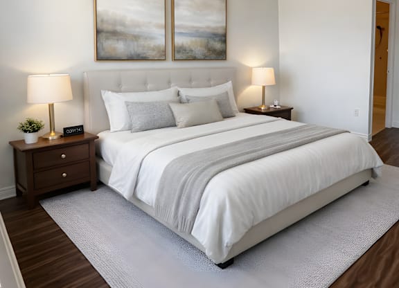 A bedroom with a large bed, two lamps, and two framed pictures on the wall.