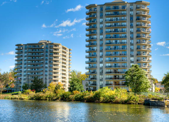 Two tall residential buildings are situated next to a body of water.