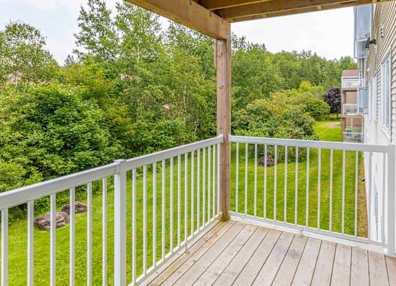 A wooden deck with a white railing overlooks a lush green yard.