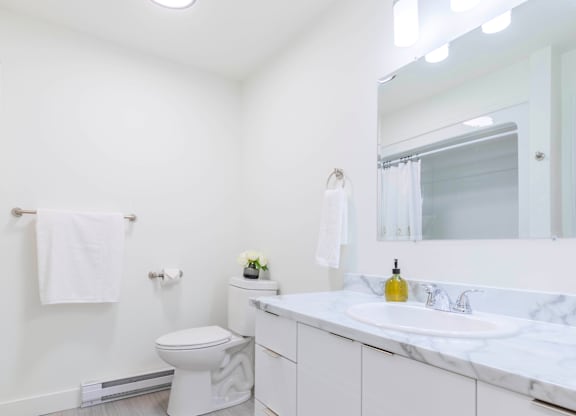 A white bathroom with a toilet, sink, and mirror.