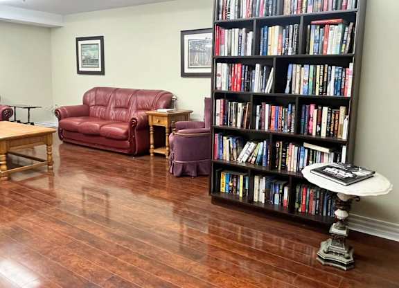 A room with a red couch, a wooden table, a chair, a bookshelf, and a round table with a book on it.