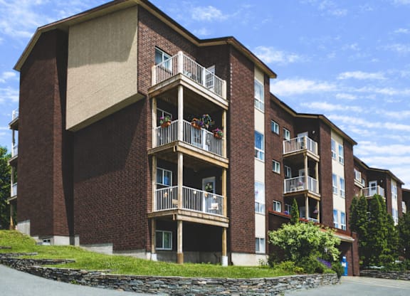 A large brick building with balconies and a stone wall in front.