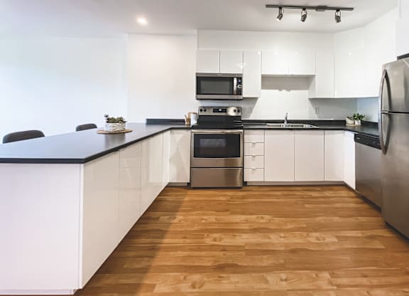 A modern kitchen with wooden floors and stainless steel appliances.