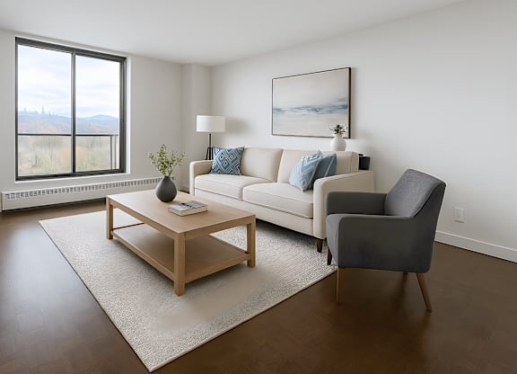 A living room with a white couch, a grey armchair, a wooden coffee table, and a large window.