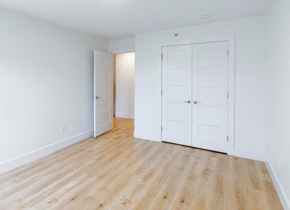 A room with white walls and wooden flooring, featuring a white door and a white closet.