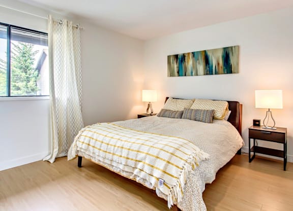 A bedroom with a bed, two lamps, and a painting on the wall.