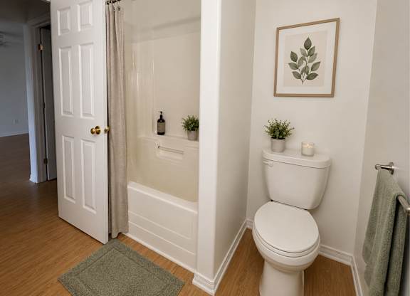 A white toilet in a bathroom with a green rug and a framed plant on the wall.