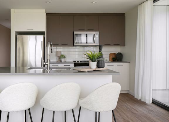 A modern kitchen with white chairs and brown cabinets.