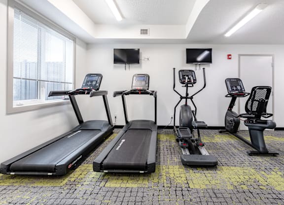 A gym with treadmills, exercise bikes, and a television.