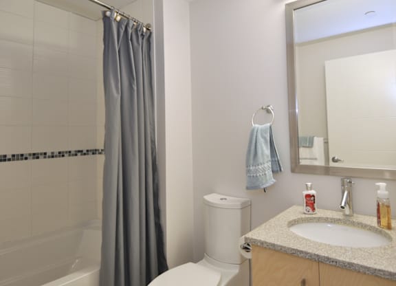 A bathroom with a white toilet, a sink, a mirror, and a shower with a grey curtain.