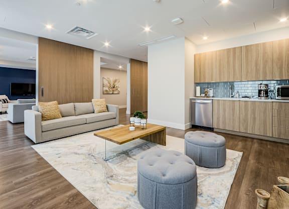 A modern living room with a grey ottoman and a wooden coffee table.