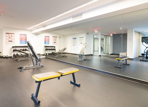 A gym with a variety of equipment including a bench, weights, and a mirror.
