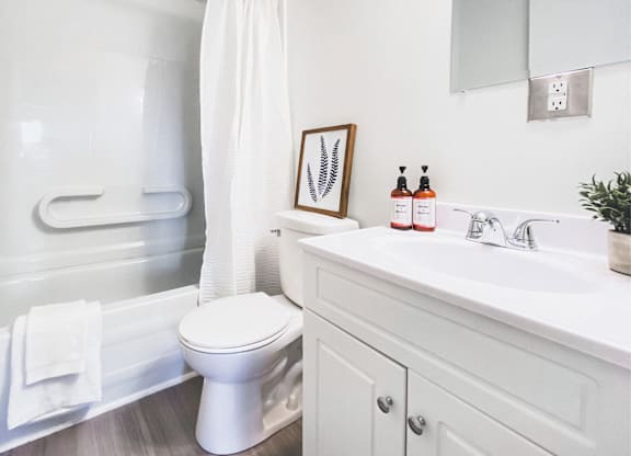 A white bathroom with a toilet, sink, and a plant.