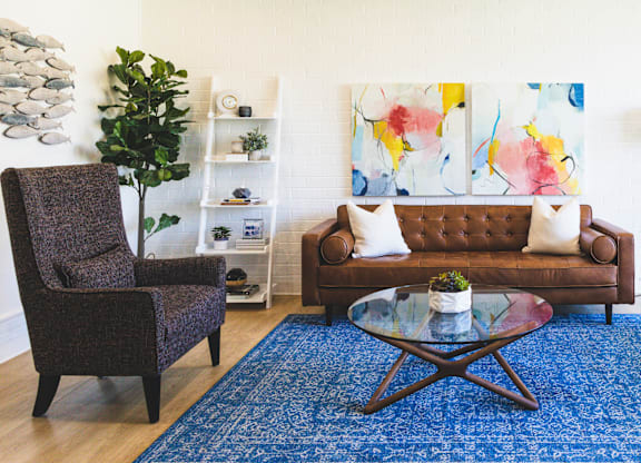 A living room with a brown couch, a brown chair, a glass coffee table and a blue rug.